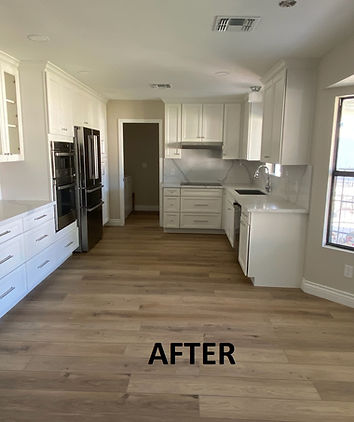 Renovated kitchen with white cabinets, light wood flooring, stainless steel appliances, and a large window.