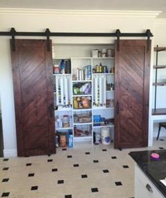 Kitchen pantry with open sliding barn doors, revealing shelves stocked with various food items and household supplies.