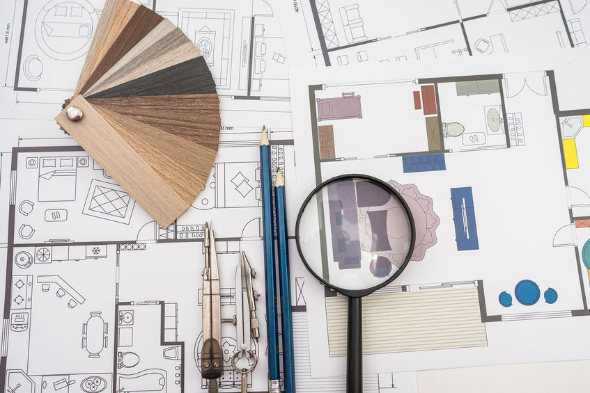 Floor plans with a magnifying glass, color palette, pencils, and compasses arranged on a table.