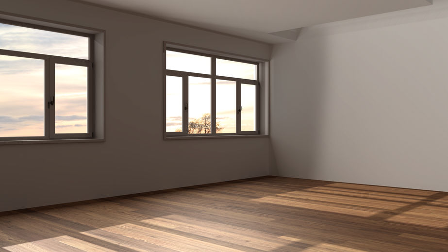 Empty room with wooden floors, large windows, and soft natural light coming through, creating shadow patterns on the floor.